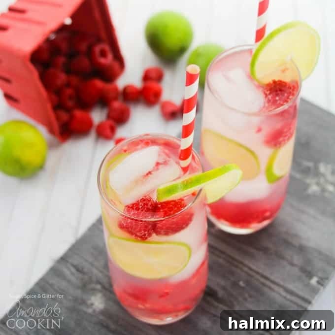 Vibrant raspberry summer cocktail served in a glass with lime slices and fresh raspberries.