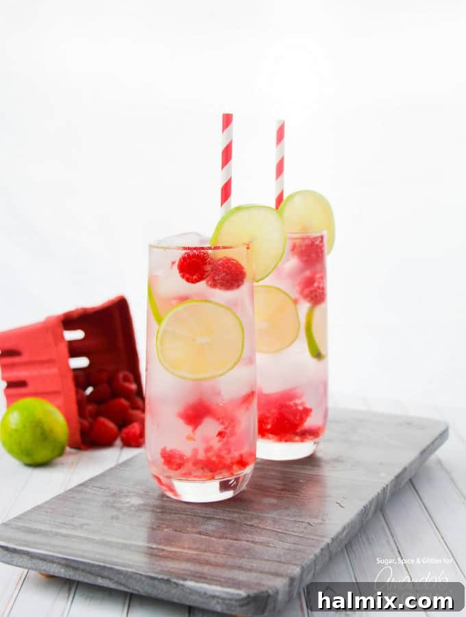 Beautifully arranged cocktail in a glass with colorful paper straws, fresh lime, and ripe raspberries, ready to serve.