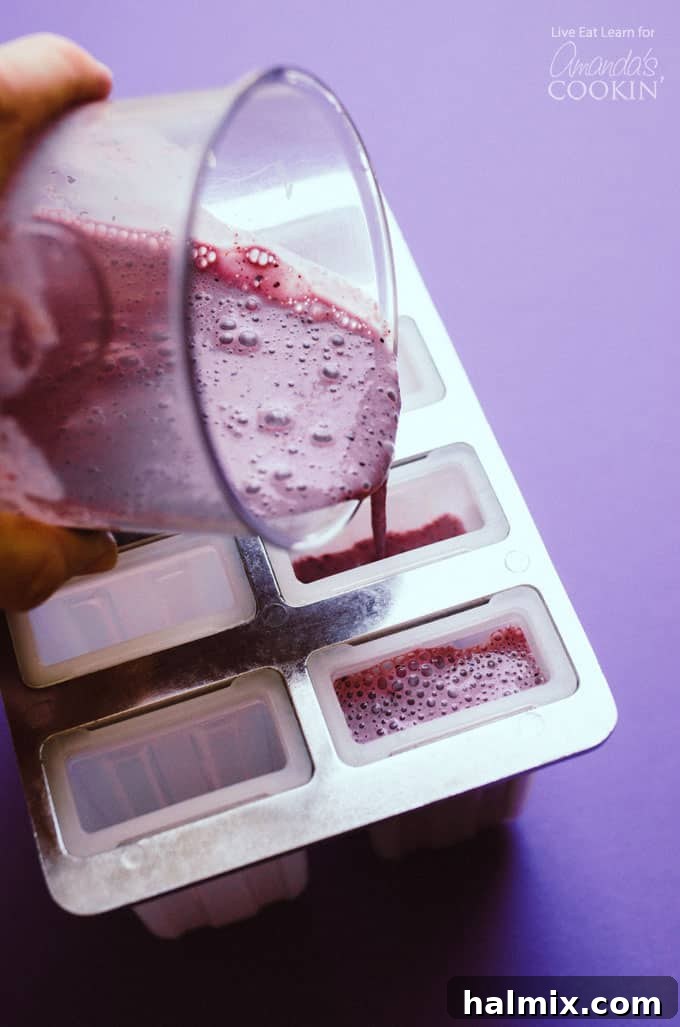 Pouring blueberry cheesecake popsicle mixture into a popsicle mold for easy preparation Pouring blueberry cheesecake popsicle mixture into a popsicle mold