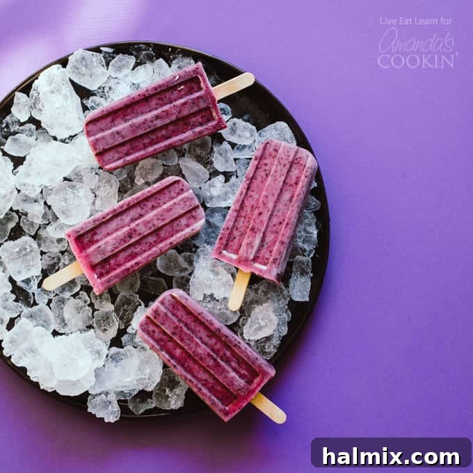Healthy and delicious Blueberry Cheesecake Popsicles, perfect for a summer treat Overhead shot of freshly made blueberry cheesecake popsicles on a plate of ice