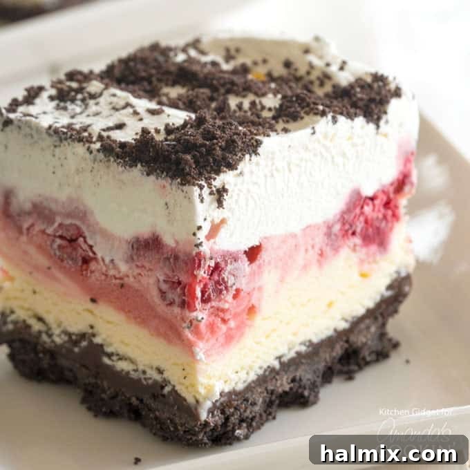 A perfectly portioned slice of Raspberry Ice Cream Delight served on a white plate, revealing its beautiful, distinct layers.