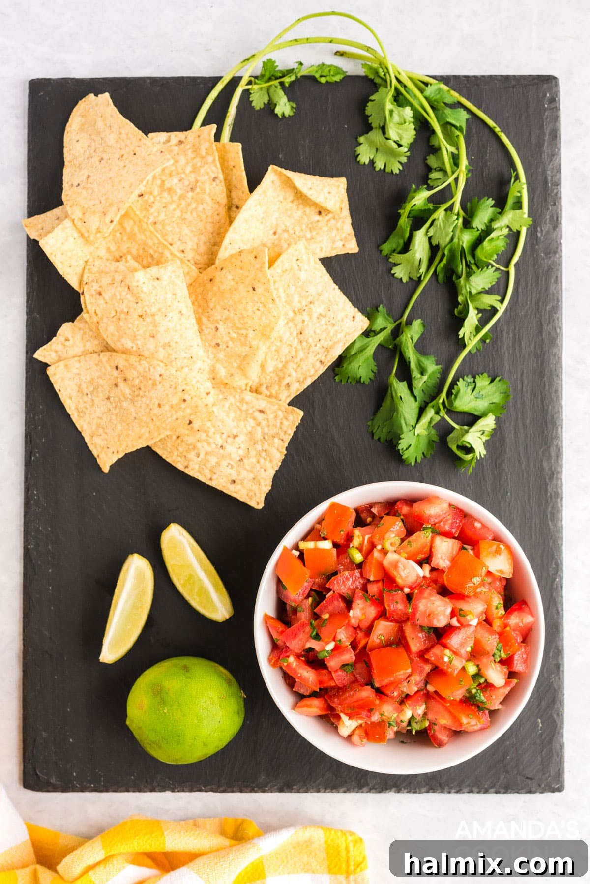 A vibrant bowl of Salsa Fresca (Pico de Gallo) rests on a dark wooden board, surrounded by crisp tortilla chips, fresh cilantro sprigs, and bright lime wedges, ready for dipping and enjoyment.