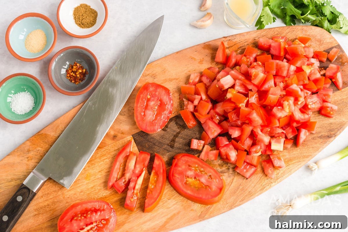 Close-up of freshly chopped ripe tomatoes with a chef's knife resting beside them on a wooden cutting board, ready for salsa preparation.