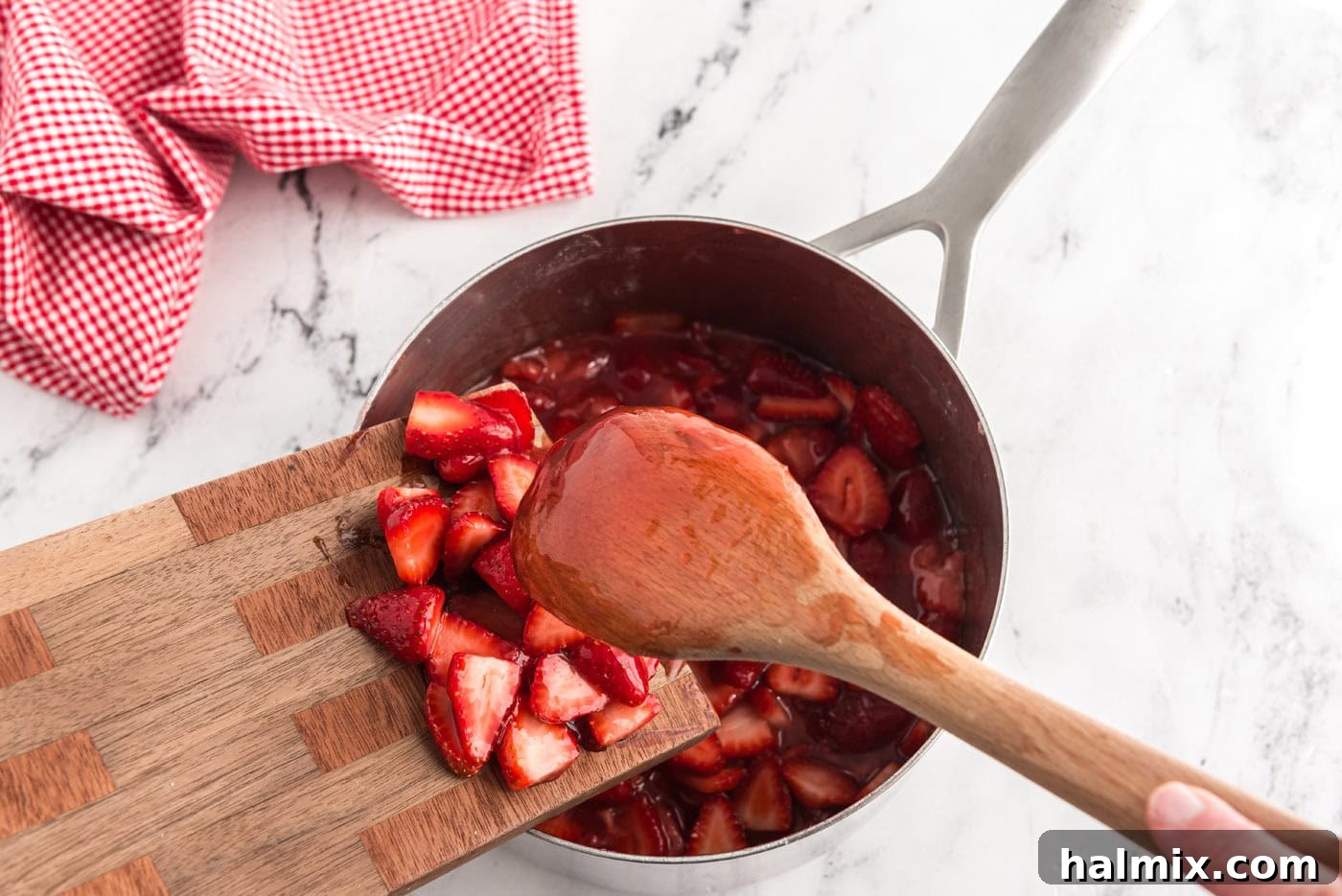 adding a quart of strawberries to homemade strawberry sauce in a saucepan