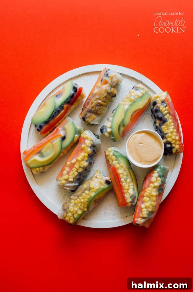 These Mexican style summer rolls are an excellent choice for appetizers, a healthy snack, or a light and satisfying meal prep option! Close-up of freshly prepared Mexican style summer rolls artfully arranged on a white plate, ready for serving. A small bowl of creamy, smoky chipotle dipping sauce sits prominently in the foreground.