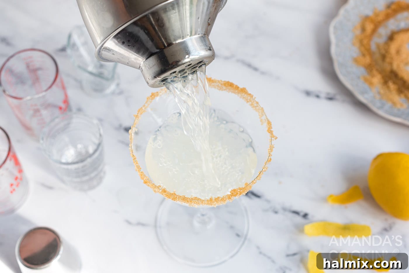 Pouring a freshly shaken Lemon Drop cocktail from a shaker into a martini glass.