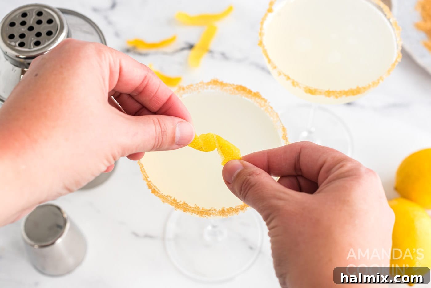 A hand twisting a lemon peel over a freshly poured Lemon Drop cocktail for garnish.