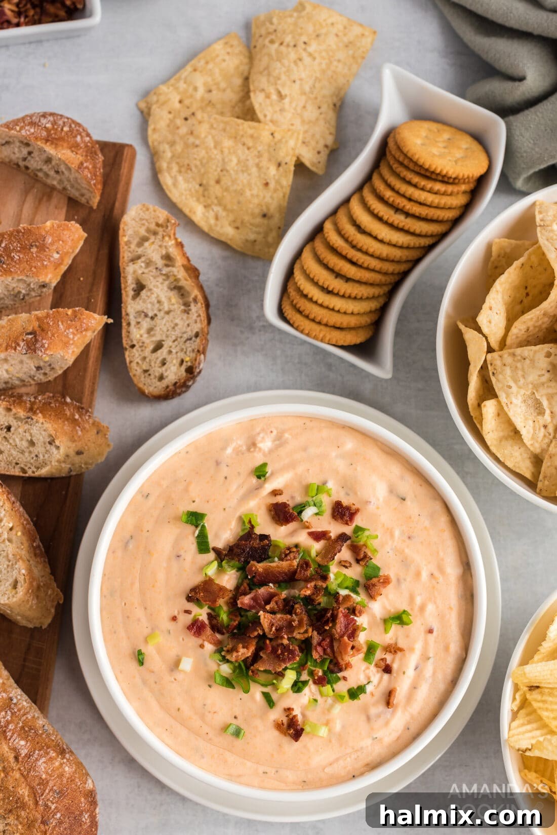 Close-up of Crockpot Cheese Dip, golden and creamy, served in a white bowl with an assortment of crackers and pretzels on the side.