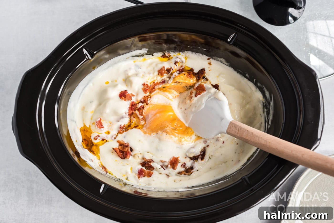 A wooden spoon stirs the melting cheese dip in the crockpot, showing its creamy texture during cooking.