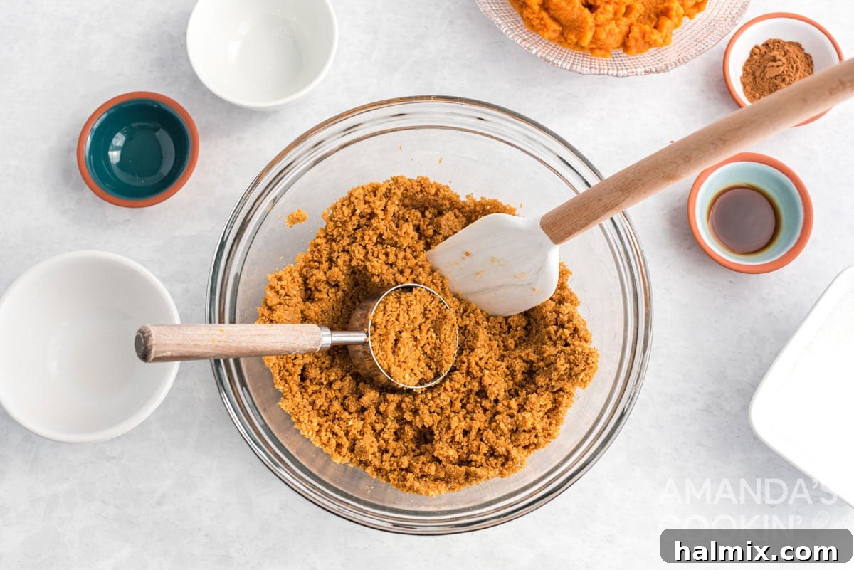Effortless Pumpkin Cheesecake 4 A bowl containing the perfectly mixed graham cracker crumb mixture, ready for pressing into the pan, with a spatula and measuring cup nearby.