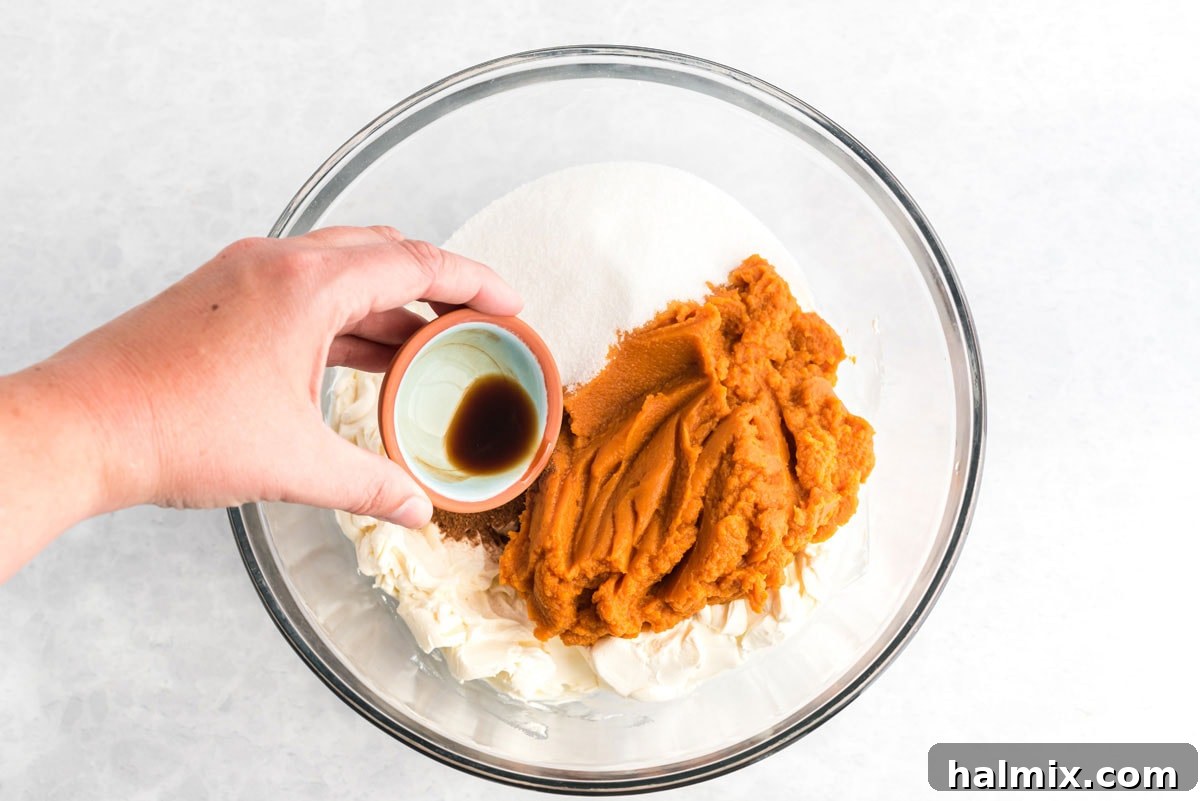 Effortless Pumpkin Cheesecake 6 Adding pumpkin puree and other filling ingredients to a bowl with softened cream cheese, ready for mixing.