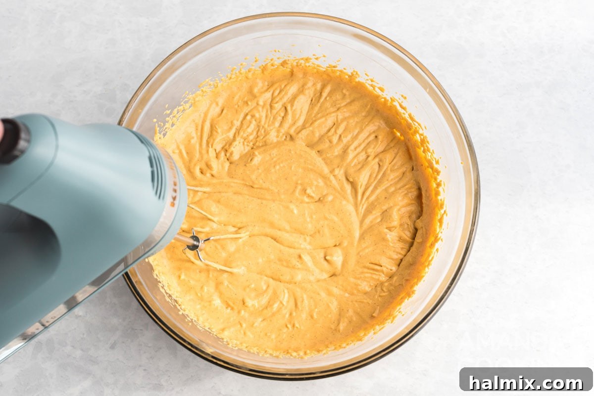 Effortless Pumpkin Cheesecake 7 An electric mixer actively blending the cream cheese, pumpkin, sugar, spice, and vanilla into a smooth, creamy cheesecake batter.