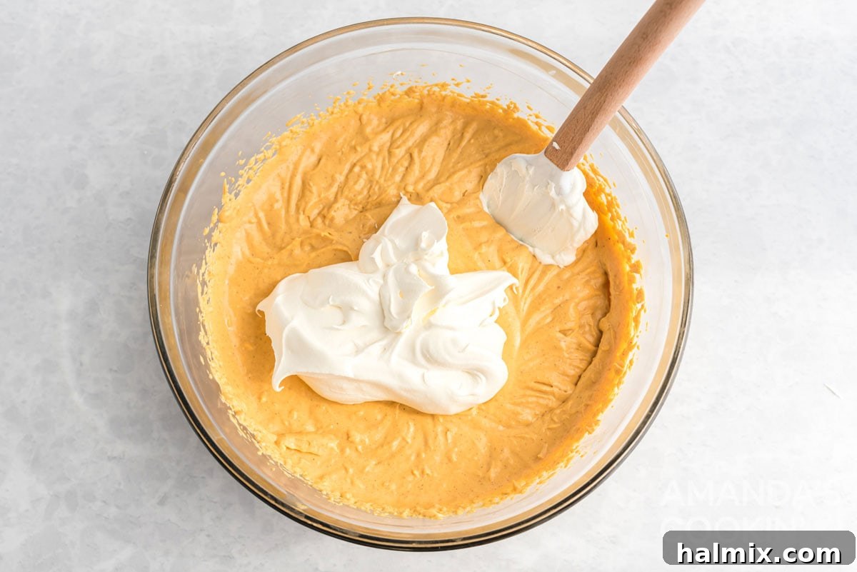Effortless Pumpkin Cheesecake 8 Creamy whipped topping being folded into the pumpkin cheesecake batter with a spatula, creating a light and airy consistency.