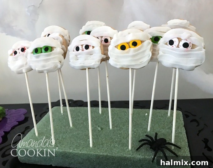 If you need Halloween food ideas for your Halloween party, be sure to check out all these sweet, savory and beverage ideas! Something for everyone. #halloweenrecipes #halloweenfoodideas #halloweenfood #halloweentreats #halloweenpartyfood #mummycookies #mozarellaeyeballs #spidertacodip #spidercookies #ricekrispypumpkins #ricekrispymonsters #dipinapumpkin #halloweenparty Mummy cookies on lollipop sticks displayed in styrofoam