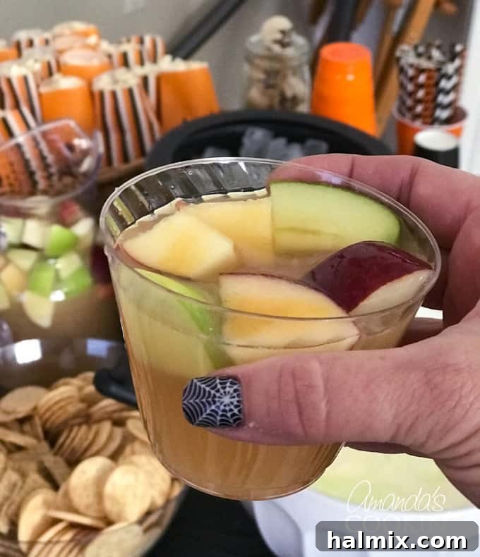 If you need Halloween food ideas for your Halloween party, be sure to check out all these sweet, savory and beverage ideas! Something for everyone. #halloweenrecipes #halloweenfoodideas #halloweenfood #halloweentreats #halloweenpartyfood #mummycookies #mozarellaeyeballs #spidertacodip #spidercookies #ricekrispypumpkins #ricekrispymonsters #dipinapumpkin #halloweenparty Close-up of Caramel Apple Sangria with ice and apple slices