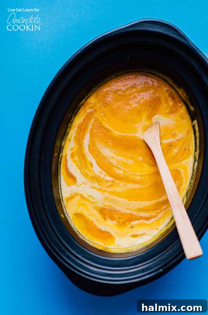 Easy Slow Cooker Butternut Squash Soup for Fall and Winter Slow Cooker Butternut Squash Soup in crockpot with wooden spoon, garnished with fresh herbs