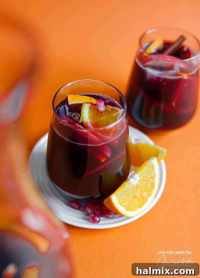 Festive Pomegranate Sangria for Holiday Gatherings Glass of pomegranate sangria with orange slice, a festive and refreshing drink perfect for holiday parties and entertaining.