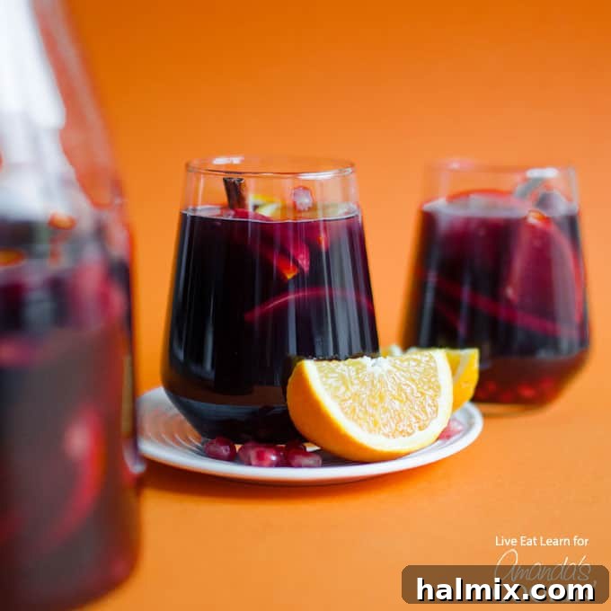 This Pomegranate Sangria is a must-try for holiday gatherings! Closeup of a glass of pomegranate sangria garnished with an orange wedge, highlighting the vibrant colors and fresh fruit.