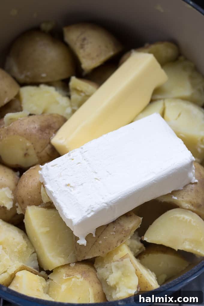 Cream cheese and butter cubes added to the hot, drained potatoes in a pot.