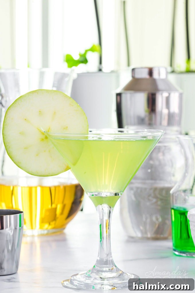Perfectly Sweet and Tart Appletini A vibrant Appletini in a classic martini glass, with fresh apples and ingredients artfully blurred in the background, emphasizing its fresh, appealing nature.