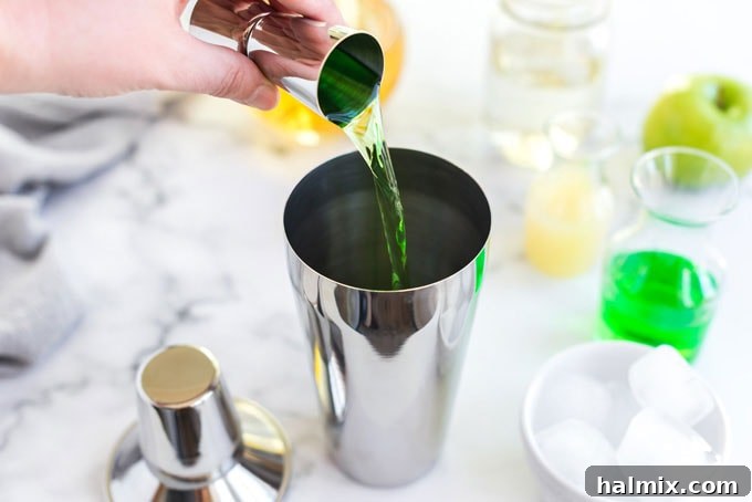 Apple Elixir 3 Pouring crisp apple vodka into a cocktail shaker filled with ice, setting the foundation for the Appletini.