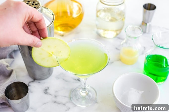 Apple Elixir 7 A crisp apple wheel slice is carefully placed on the rim of the martini glass, adding an elegant and fresh garnish to the Appletini.
