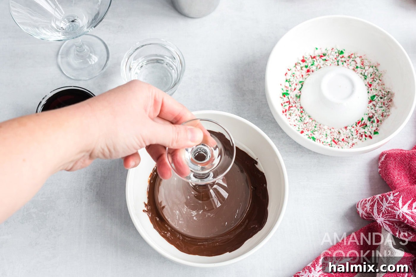 A hand dipping a martini glass rim into melted chocolate for garnish.