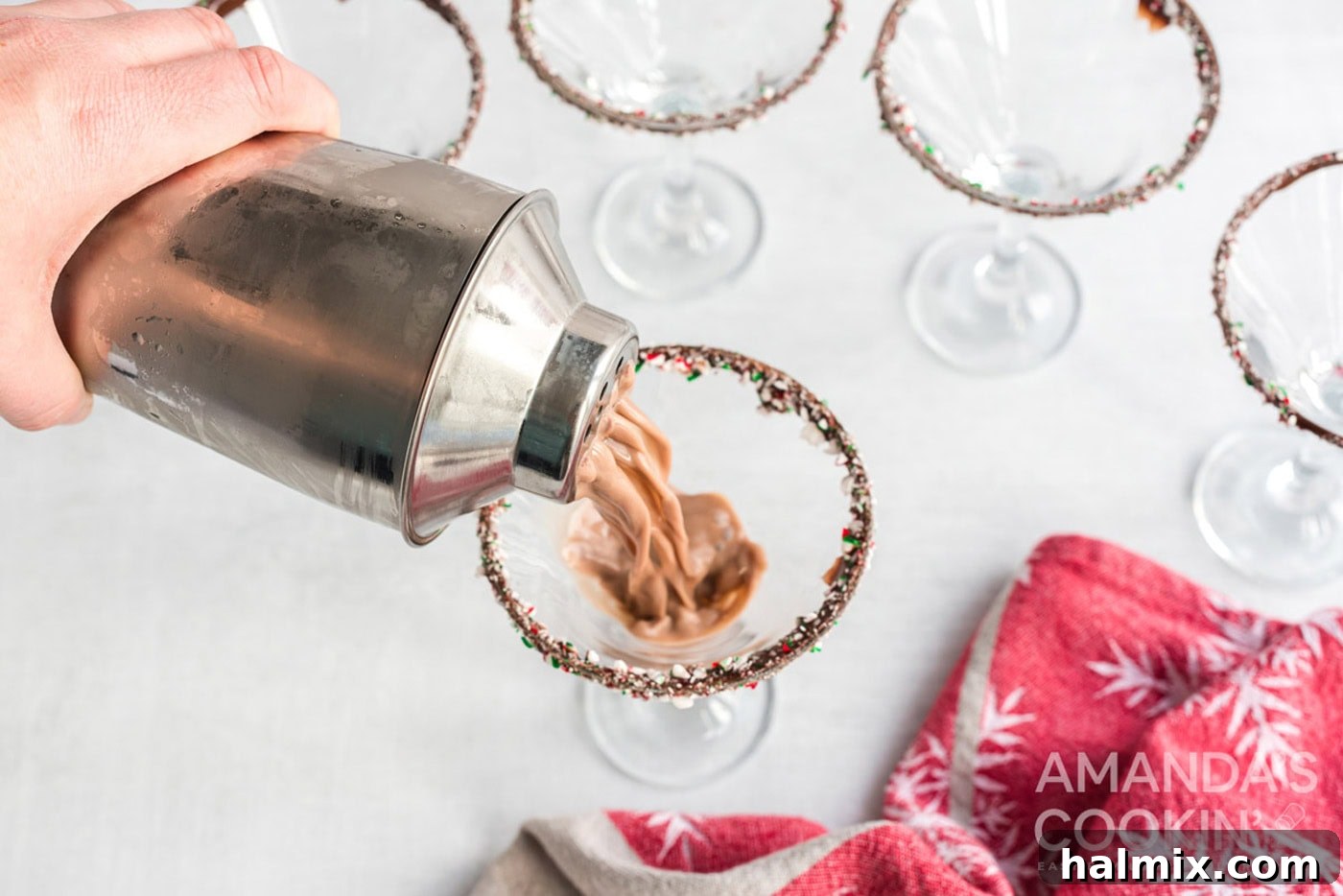 A freshly shaken chocolate peppermint cocktail being poured into a garnished martini glass.