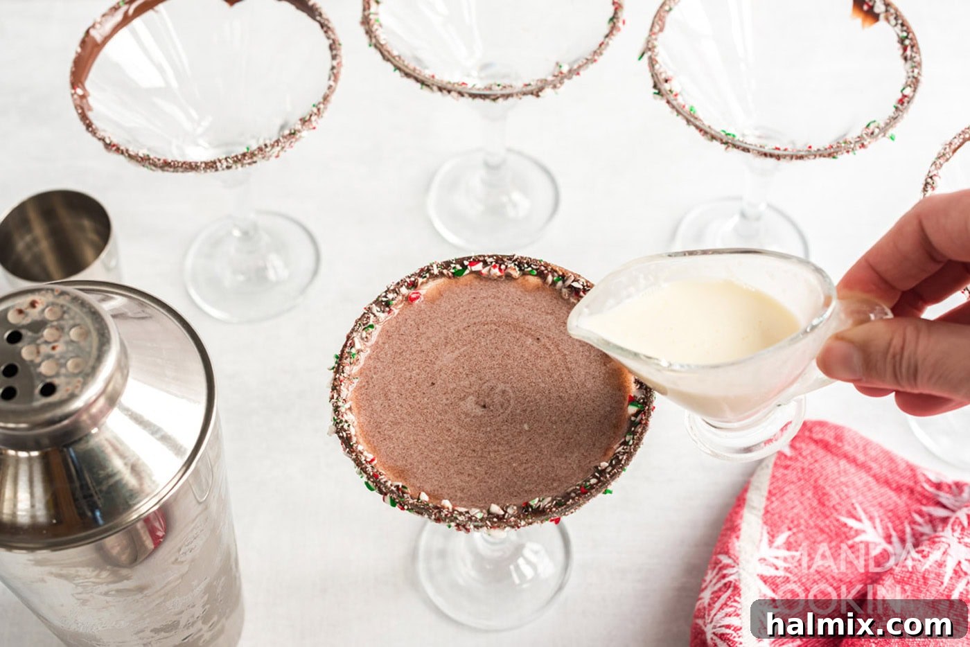 A thin stream of cream being poured onto the surface of a chocolate peppermint martini for garnish.