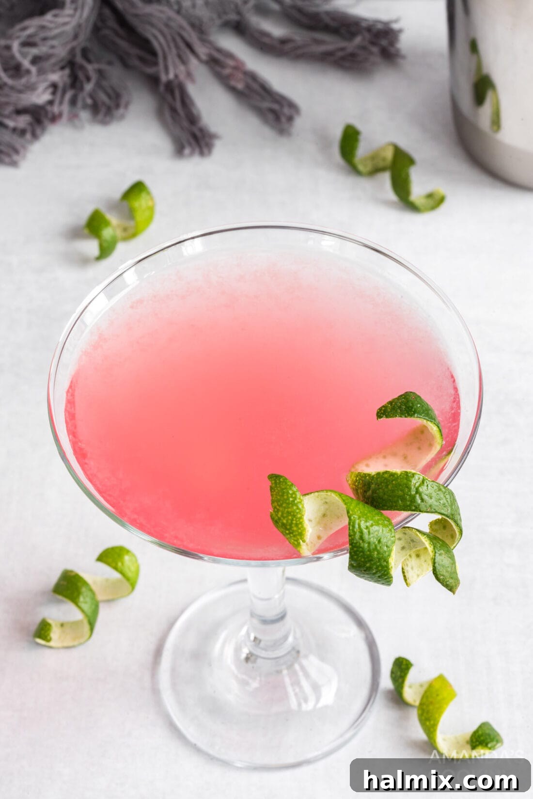 Close-up of a sparkling Cosmopolitan cocktail with a perfectly curled lime twist garnish, highlighting its appealing pink hue.