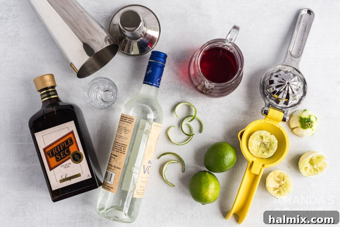 The key ingredients for a Cosmopolitan cocktail laid out: a bottle of citron vodka, Cointreau, fresh limes, and cranberry juice.