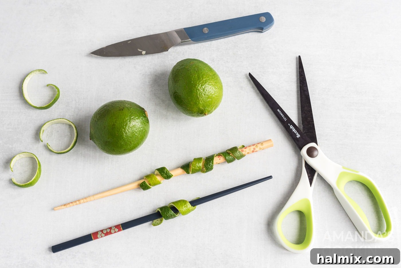 Hands using scissors to trim a lime peel, preparing a garnish for a cocktail.