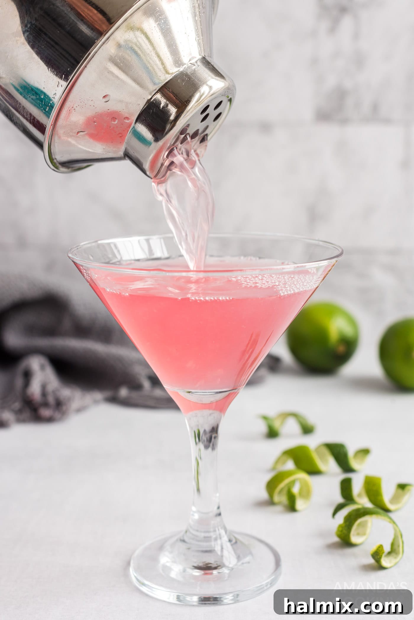 A Cosmopolitan cocktail being strained from a shaker into a martini glass, creating a smooth, inviting pour.
