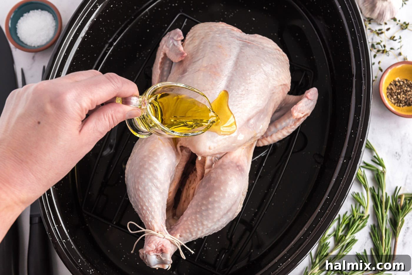 Golden Roasted Chicken 6 A stream of olive oil being poured over a raw whole chicken in a roasting pan, preparing it for seasoning and roasting.