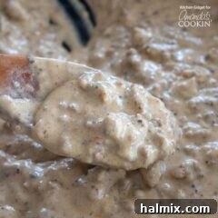 Close-up view of creamy sausage gravy in a pan with a wooden spoon, highlighting its rich texture.