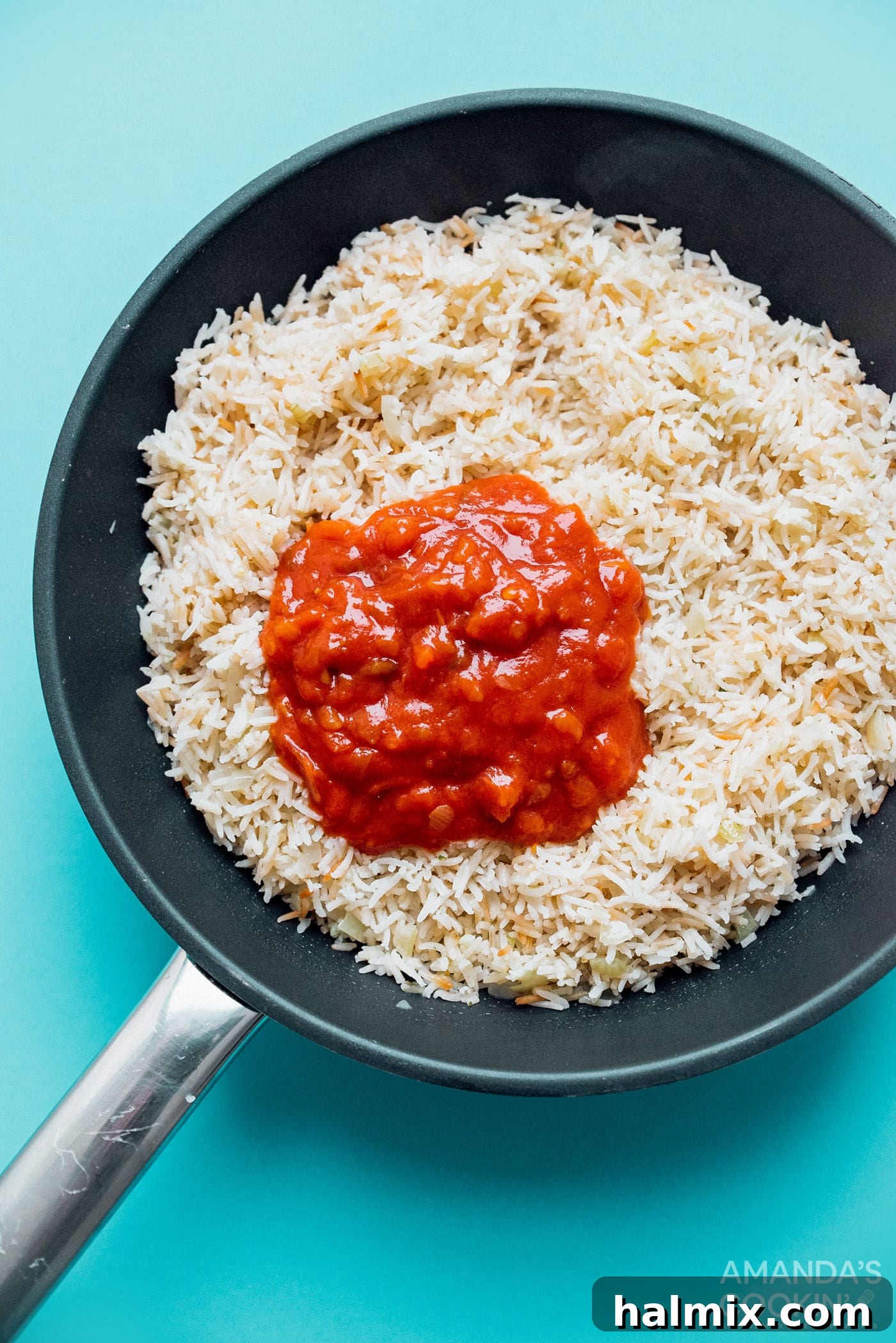 Close-up of toasted rice, chopped onions, and minced garlic in a pan before adding broth, illustrating the initial flavor-building stage of Spanish rice.