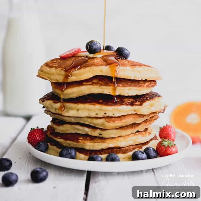 These classic buttermilk pancakes are fluffy, filling, and so delicious. Homemade pancakes are easier than you thought, so throw away that box mix! #breakfast #breakfastrecipes #buttermilkpancakes #pancakes #homemadepancakes A plate of perfectly stacked fluffy buttermilk pancakes, garnished with fresh blueberries and a drizzle of maple syrup.