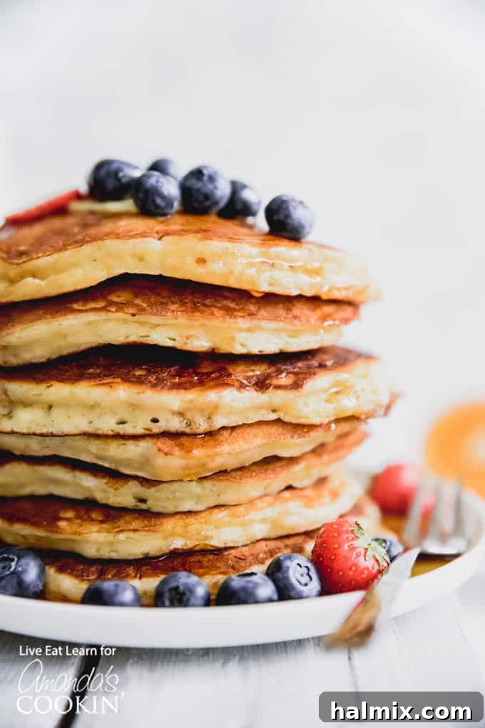 These classic buttermilk pancakes are fluffy, filling, and so delicious. Homemade pancakes are easier than you thought, so throw away that box mix! #breakfast #breakfastrecipes #buttermilkpancakes #pancakes #homemadepancakes A vibrant display of fluffy buttermilk pancakes garnished with an assortment of fresh blueberries and sliced strawberries, ready to be enjoyed.