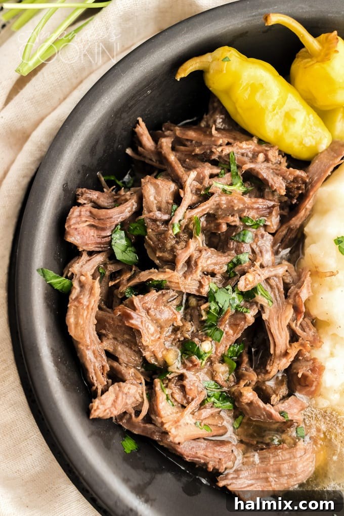 A close-up shot of shredded Mississippi Pot Roast with visible tender meat fibers and rich gravy, lifted by a fork from a serving bowl.