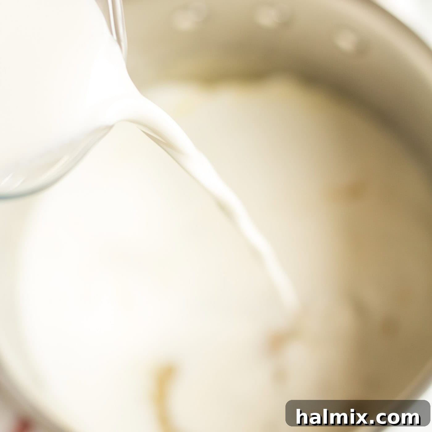 Golden-Crusted Macaroni Bake 5 Milk and heavy cream being slowly poured into the saucepan with the roux, while whisking.