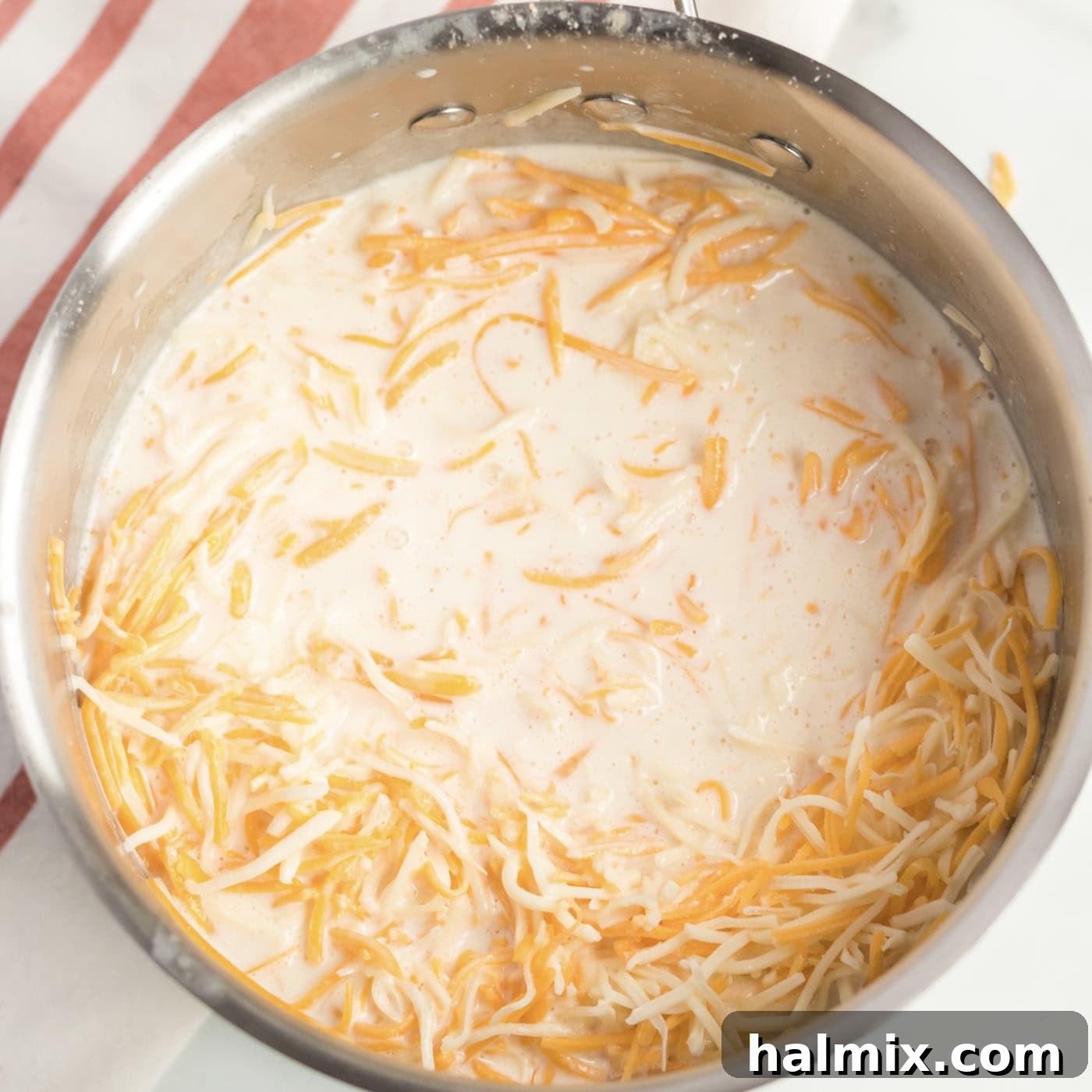 Golden-Crusted Macaroni Bake 6 Shredded cheeses being added to the creamy sauce in the saucepan, ready to be melted.