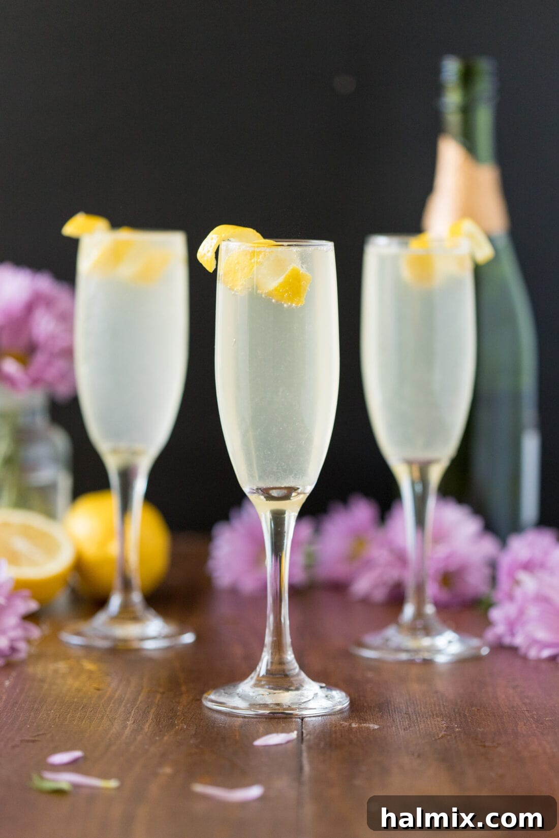 Three elegant French 75 cocktails, each adorned with a lemon twist, ready to be served in a celebratory setting.