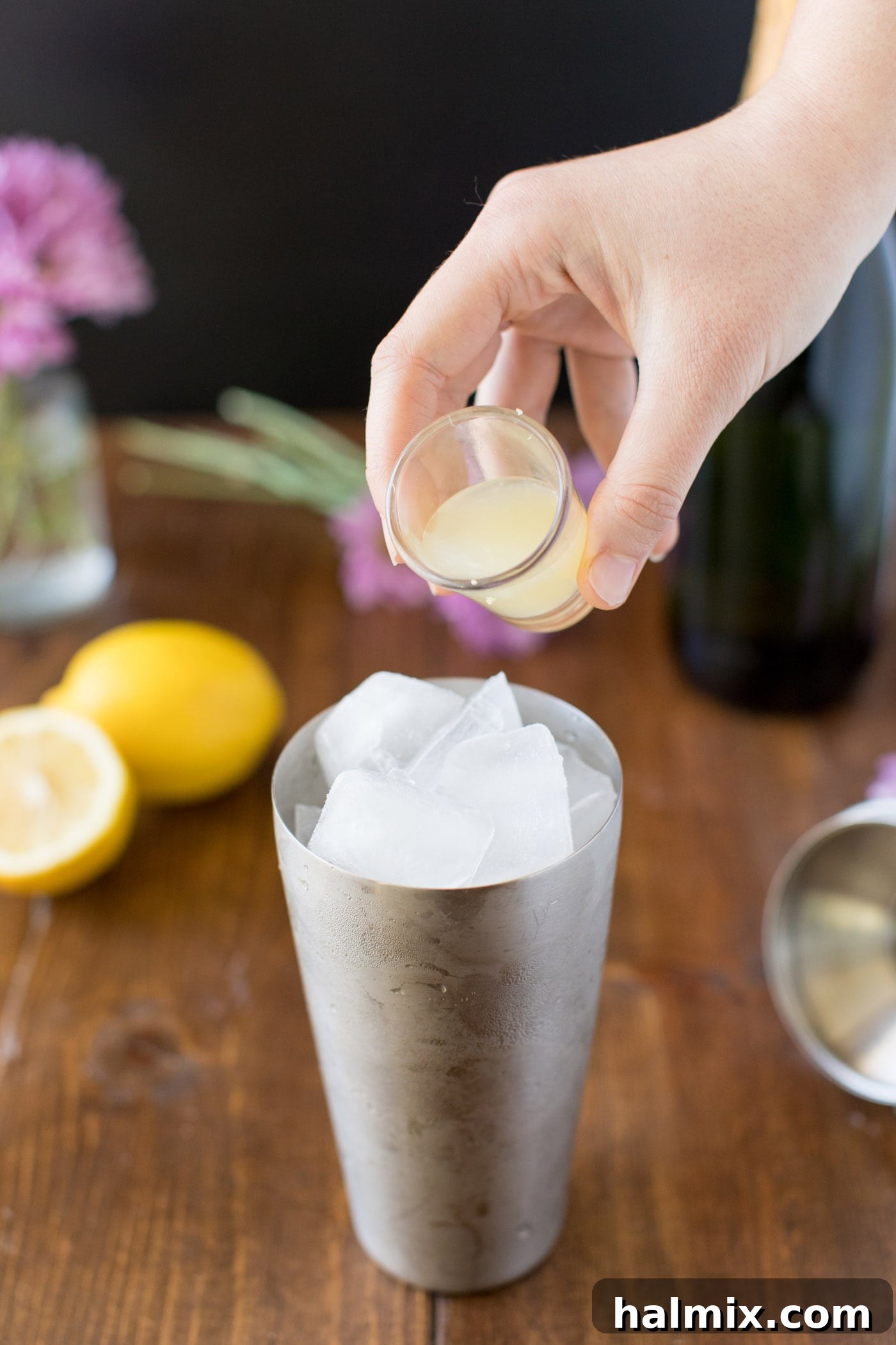 A bartender pouring freshly squeezed lemon juice into a cocktail shaker filled with ice and gin, preparing a French 75.