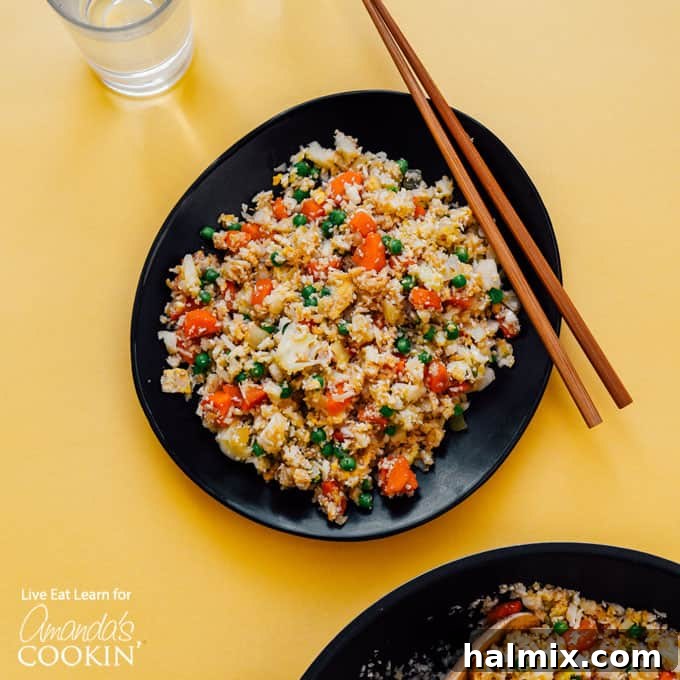 A black bowl brimming with freshly made cauliflower fried rice, accompanied by chopsticks, highlighting its appetizing texture and appealing presentation.