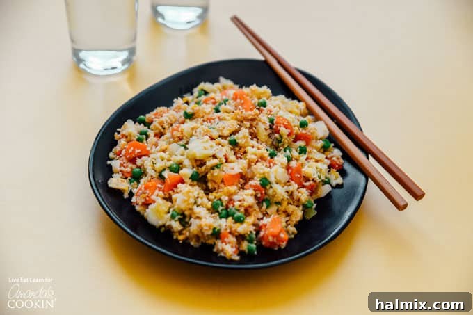 A close-up of a partially cooked Cauliflower Fried Rice mixture in a wok, showing the colorful vegetables and textured cauliflower.