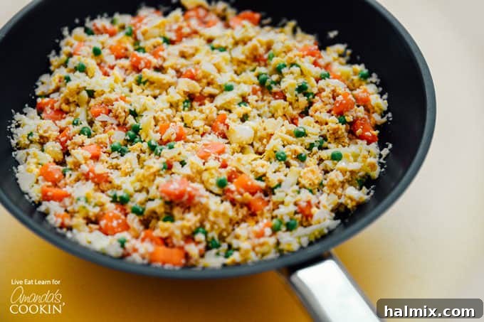 Cauliflower fried rice cooking in a wok with vegetables, showcasing the stir-frying process before adding eggs.