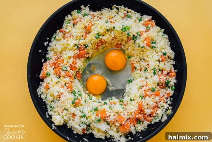 Cauliflower fried rice in a wok with scrambled egg pieces mixed in, ready for the final seasonings.