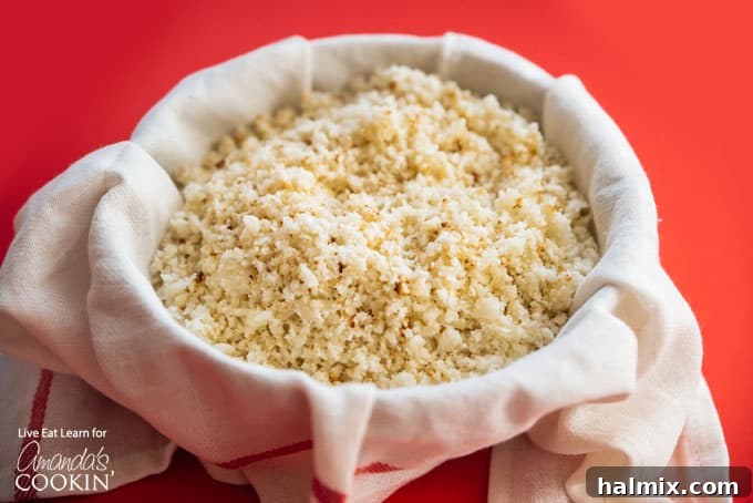 Grated cauliflower pulp being squeezed inside a cheesecloth, showing excess moisture removal.