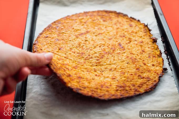 Cauliflower pizza crust being carefully lifted and flipped during baking.