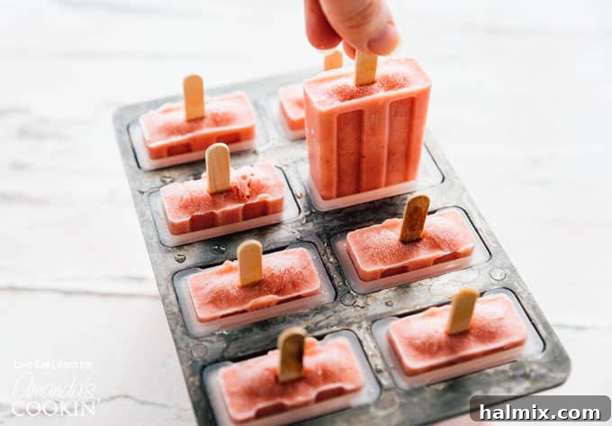 Strawberry banana popsicles partially frozen in a mold with sticks inserted.